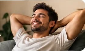 Homem sorrindo e relaxado no sofá, com as mãos atrás da cabeça